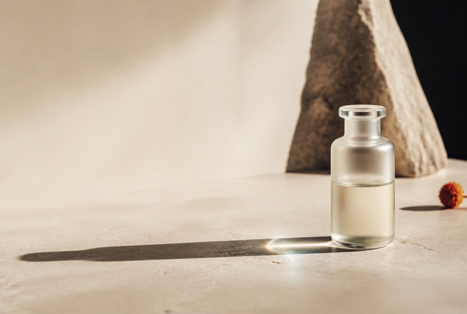 A single unmarked frosted glass vial standing on warm stone, casting one long hard-edged shadow into deep negative space